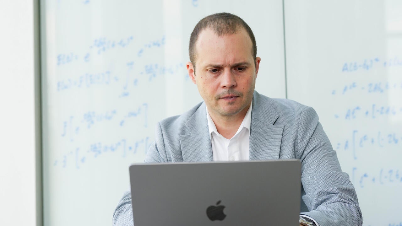 Vlad Gheorghiu works at computer seated in front of a whiteboard with equations written on it