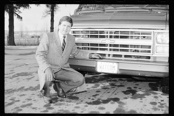 Ian McPhee kneeling beside a car with a license plate that reads "WATCOM"