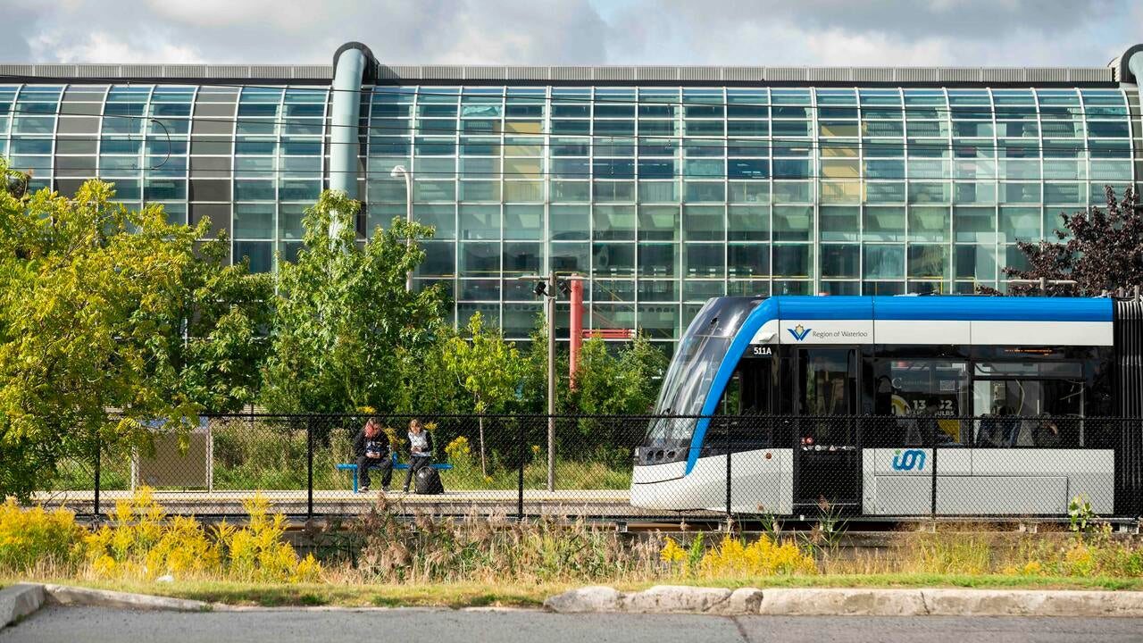 Train passes two people seated on a bench in front of the Davis Centre