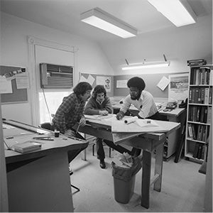 Black and white photo of students looking at papers on a desk