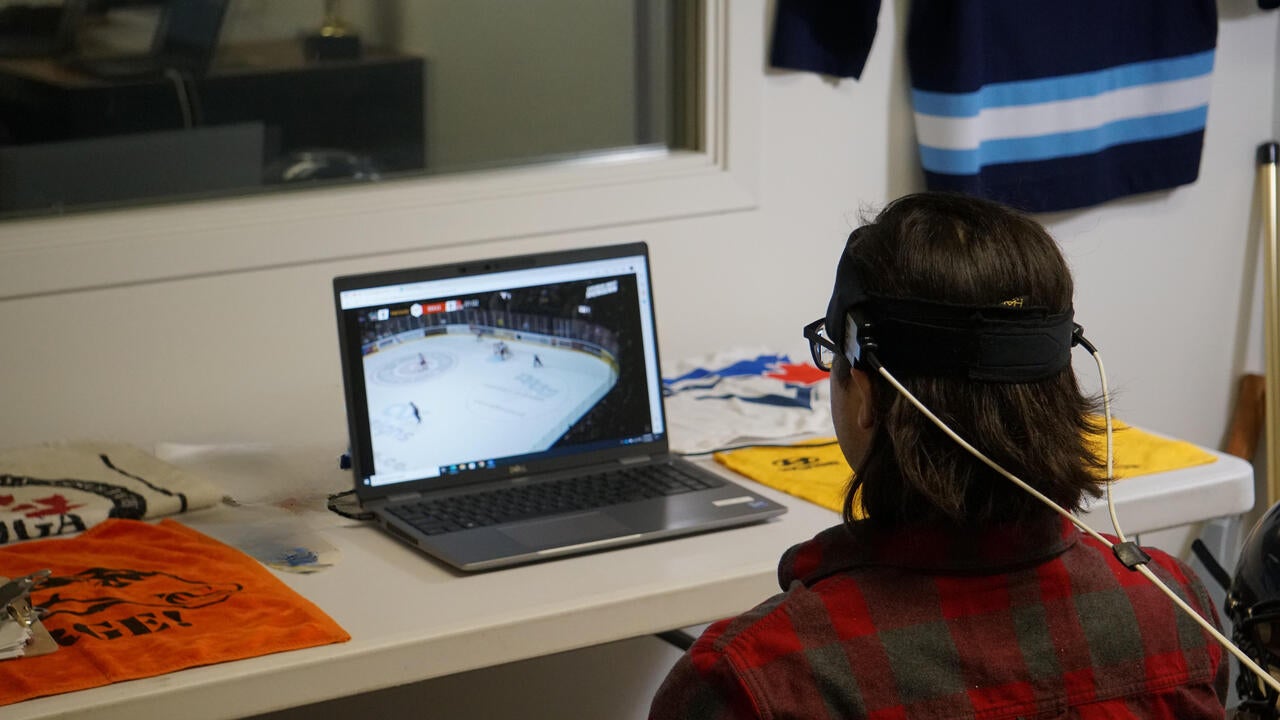 Mock setup of the non-invasive brain imaging method used in the study to analyze a participant watching a hockey game on a lapto