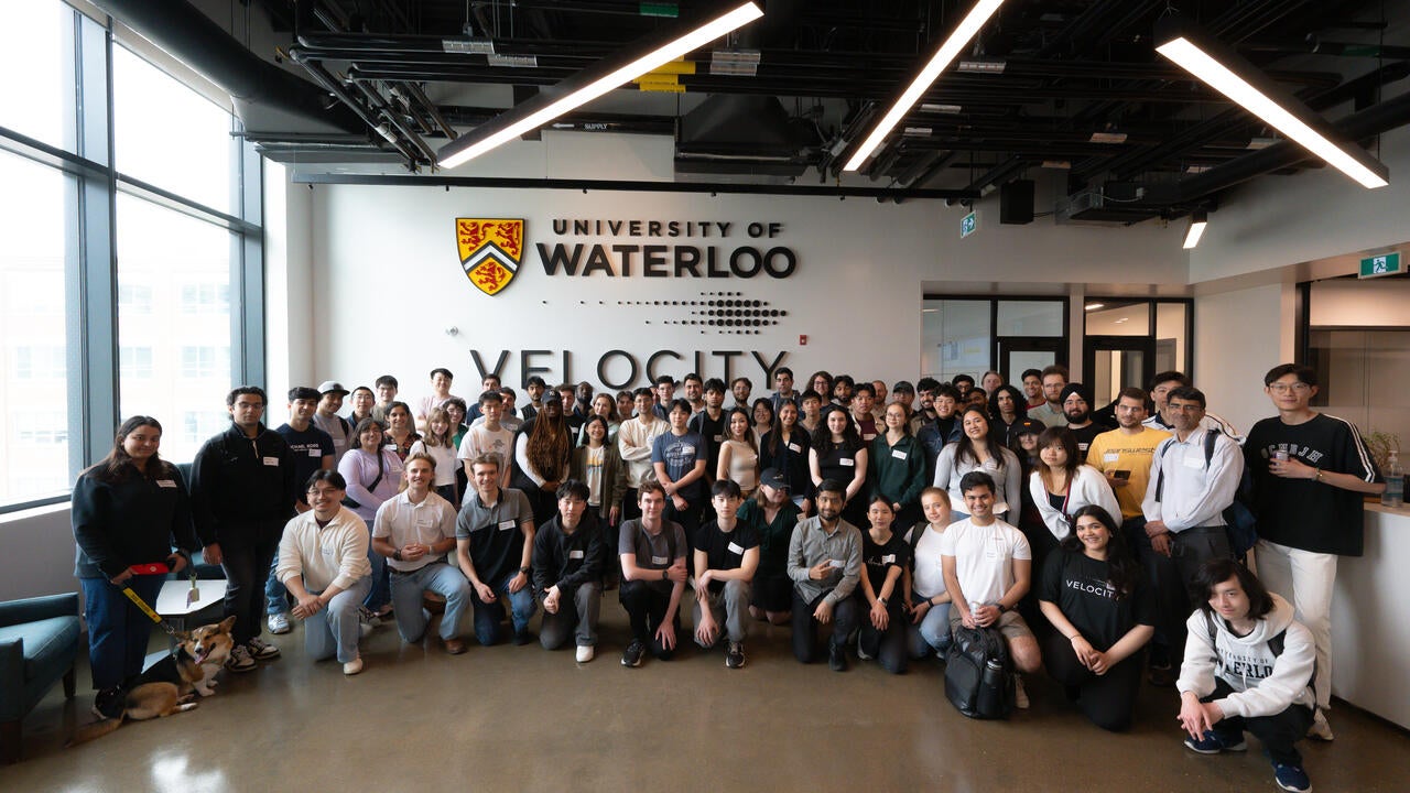 Group of people pose in front of wll featuring a University of Waterloo logo and a Velocity logo.
