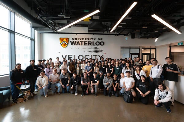 Group of people pose in front of wll featuring a University of Waterloo logo and a Velocity logo.
