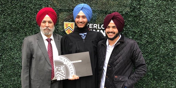 Dr. Singh, Harkanwal, and Jasmeet at Harkanwal’s graduation in front of a green background and a sign that says #UWaterlooGrad