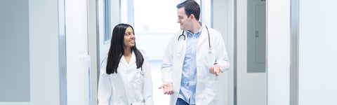 Two students in white lab coats walk along bright hall
