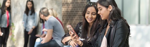 Two students sitting outside looking at a phone