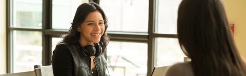 Student with headphones around their neck laugh with another student