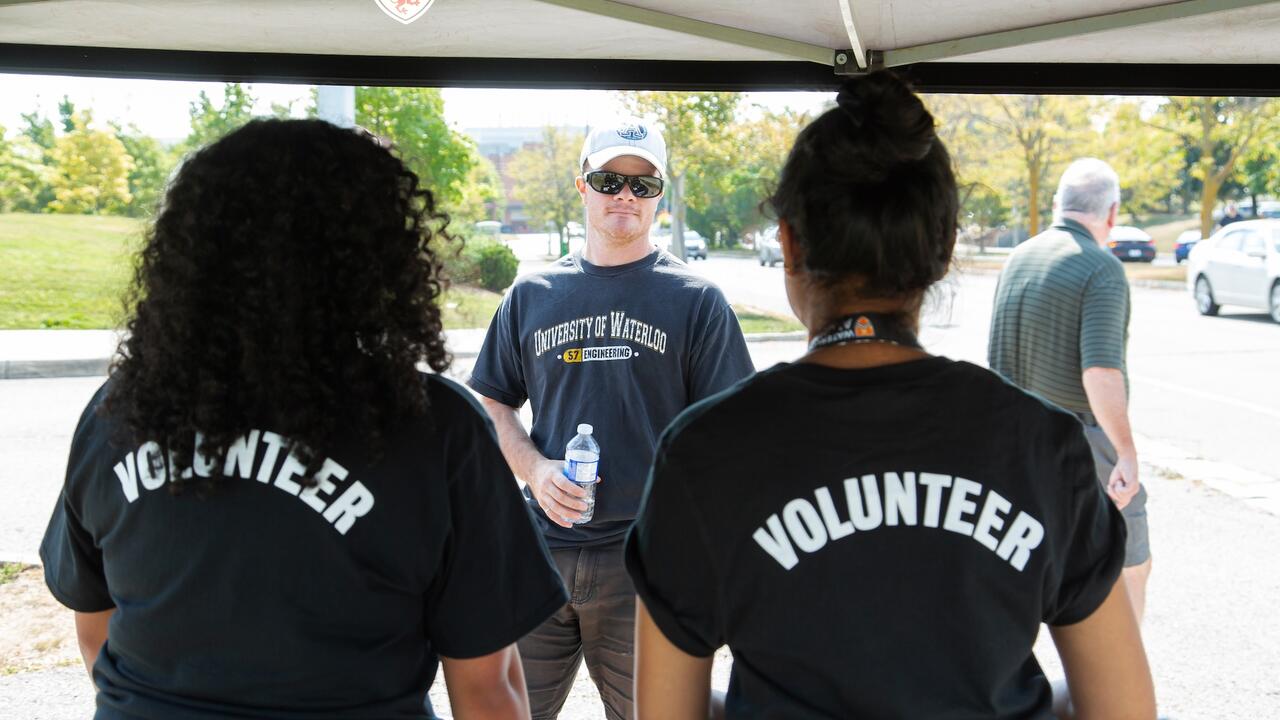 Two volunteers facing away from the camera helping an alum at an event