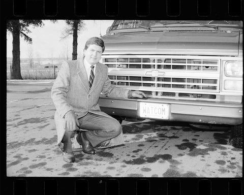 Man crouched in front of car with e WATCOM license plate