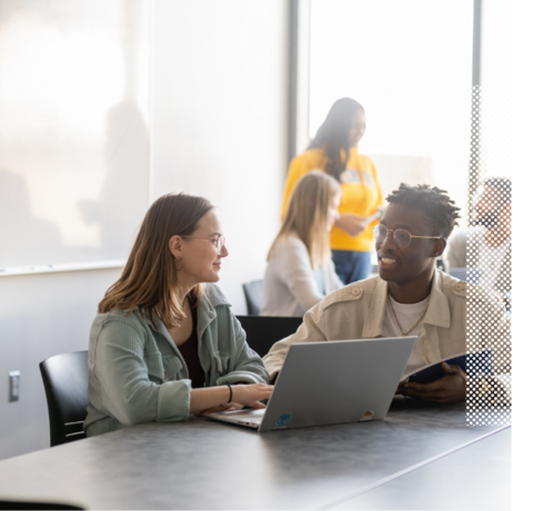 Two people talking to each other while sitting behind a laptop