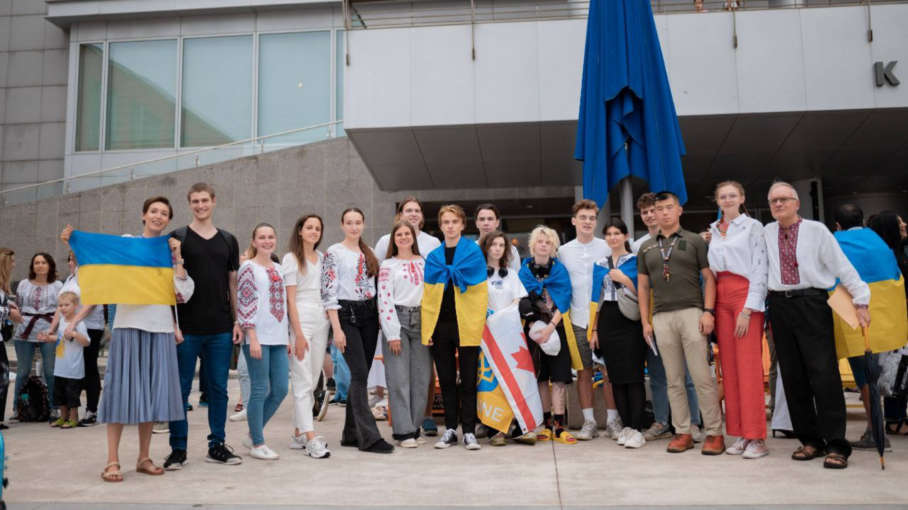 A group of students and adults pose in front of City Hall with Ukrainian flags