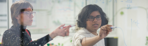 Two students work together on a transparent whiteboard